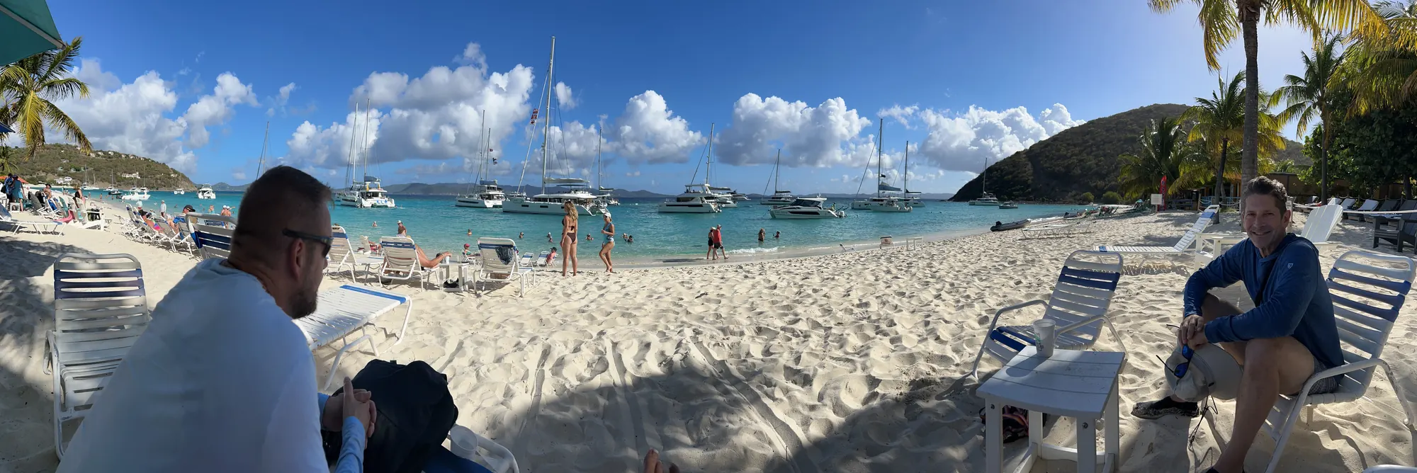 Robert relaxing on a white-sand beach bar with sailboats anchored in the bay