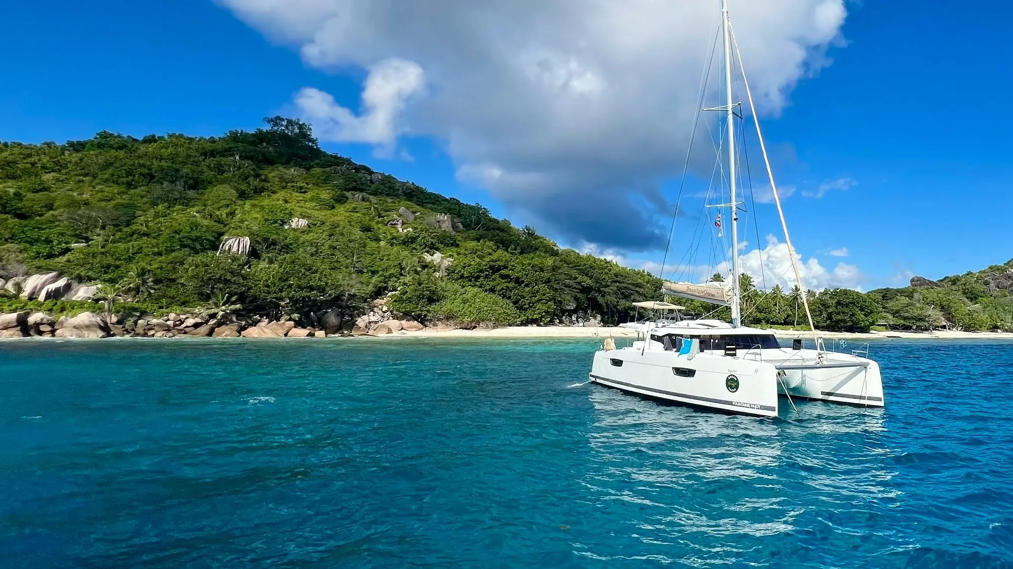 Catamaran anchored off a green island under a blue sky